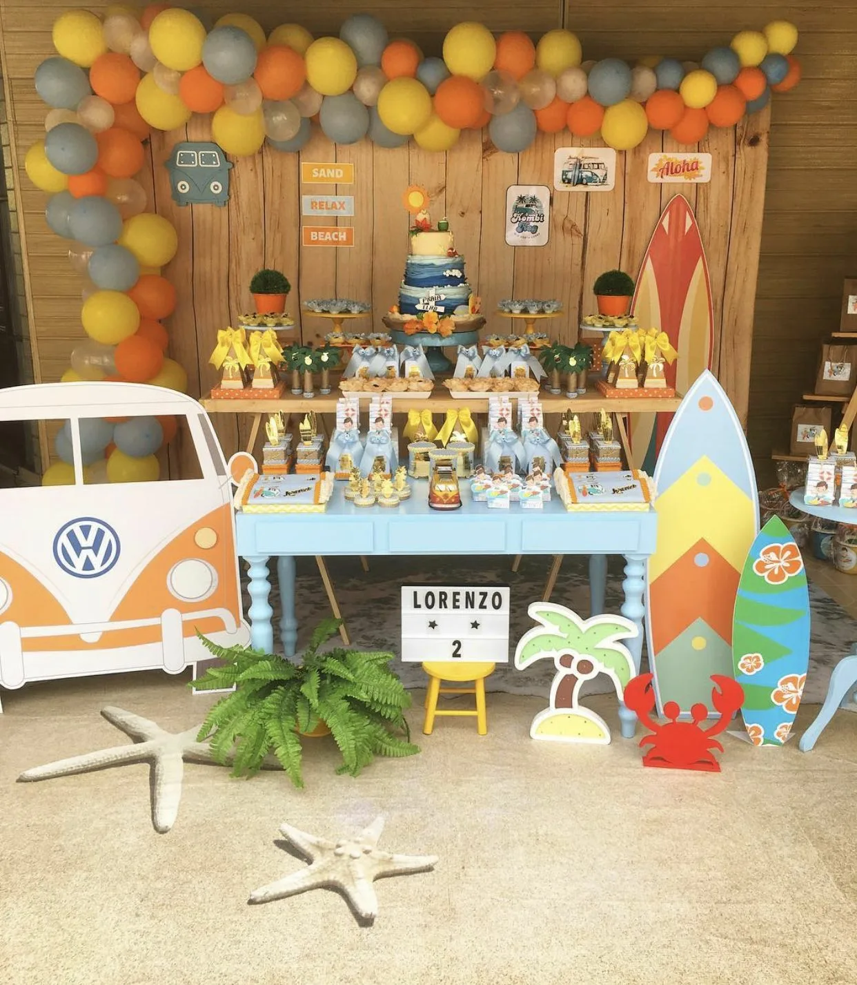 Beach Themed Birthday Cake Table With Wood Background With Surf Board Decors And Balloon